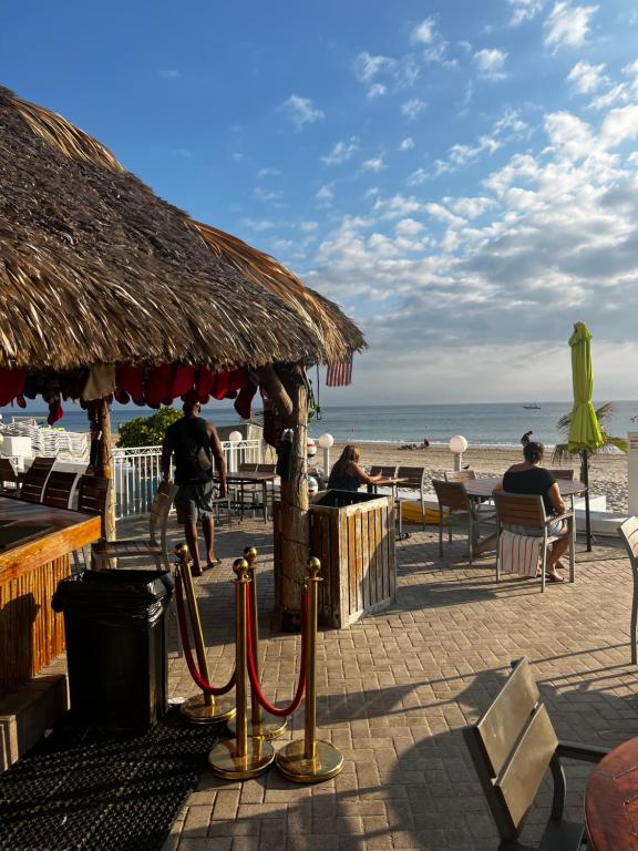 a beach with a straw umbrella and people sitting on the beach at Ocean Manor Tiki Sunset Retreat in Fort Lauderdale
