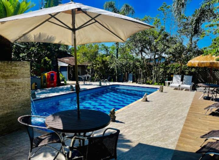 a table with an umbrella next to a swimming pool at Ganesh Chalés in Boracéia