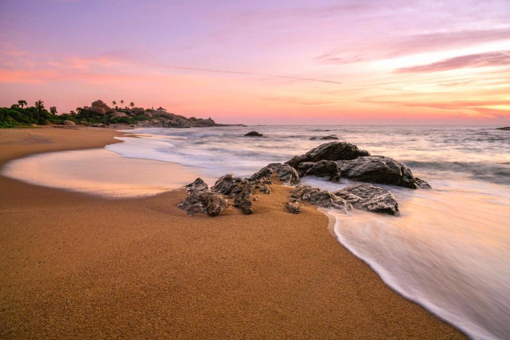 Beach Bungalow Yala في كيريندا: شاطئ فيه صخور في الماء وقت الغروب