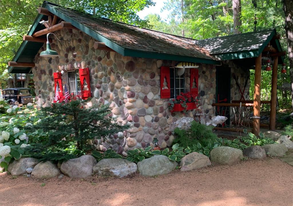 a stone cabin with red windows and flowers in front of it at The croquet cabin your year round romantic escape in Boulder Junction