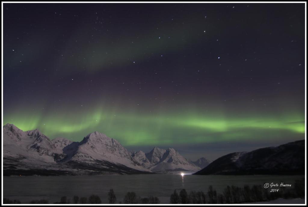 an aurora in the sky over a mountain range at Lyngen Apartments in Lyngseidet