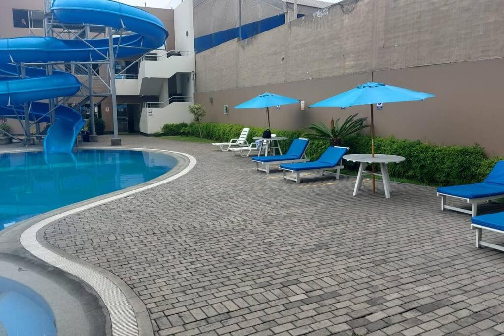 - une piscine avec des chaises et des parasols bleus à côté d'un bâtiment dans l'établissement Dpto. con piscina en San Miguel, à Lima