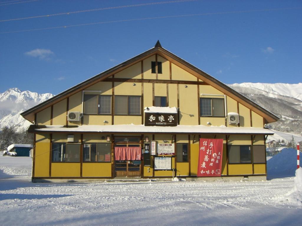 un edificio con un cartello sopra nella neve di Nagomi-tei a Hakuba