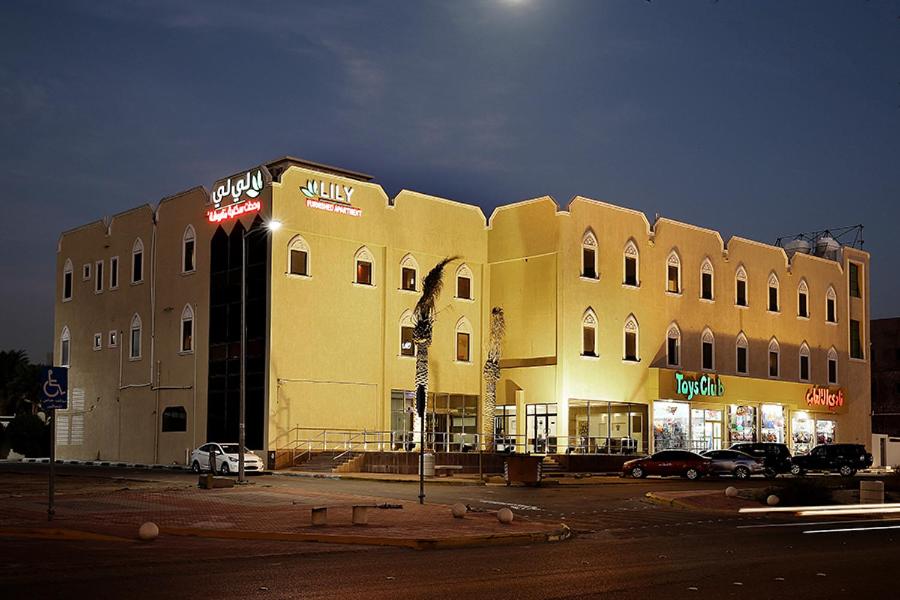 un grande edificio giallo con auto parcheggiate in un parcheggio di Lily Hotel Suite Hofuf a Al Hofuf