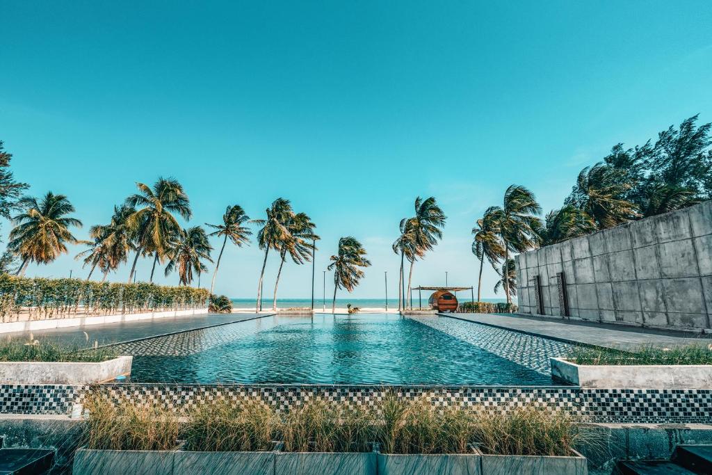 a swimming pool with palm trees and the beach at The Bloc @ Sea in Thap Sakae