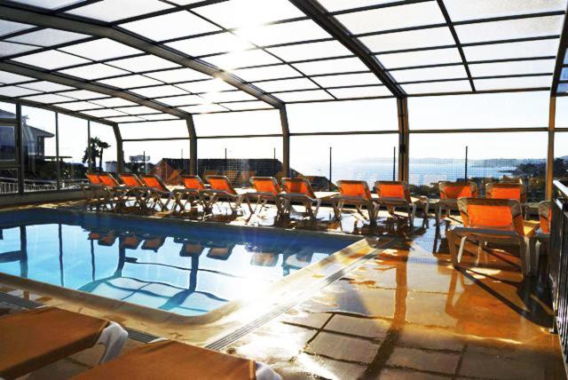 una piscina con sedie arancioni in un grande edificio di Apartamentos Riveiro a Sanxenxo