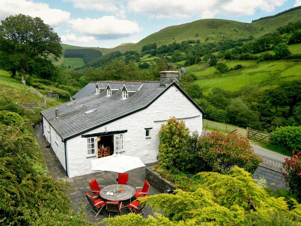 a white building with a table and chairs and an umbrella at Tyn Y Ffordd in Llanymawddwy