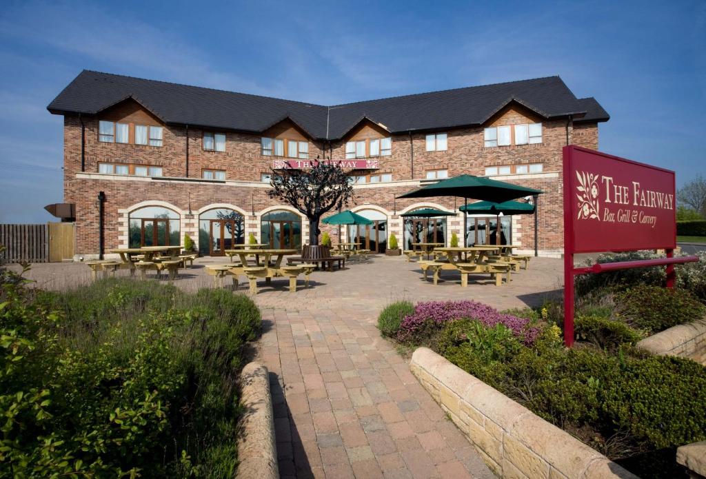 a large brick building with tables and umbrellas at The Fairway in Barnsley
