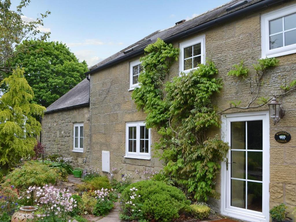a brick house with white windows and plants at Wisteria Cottage in Alnham