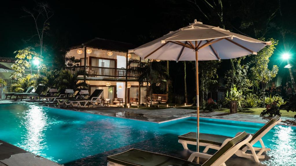 una piscina con sillas y una sombrilla junto a una casa en Pousada Recanto Caxando, en Trancoso