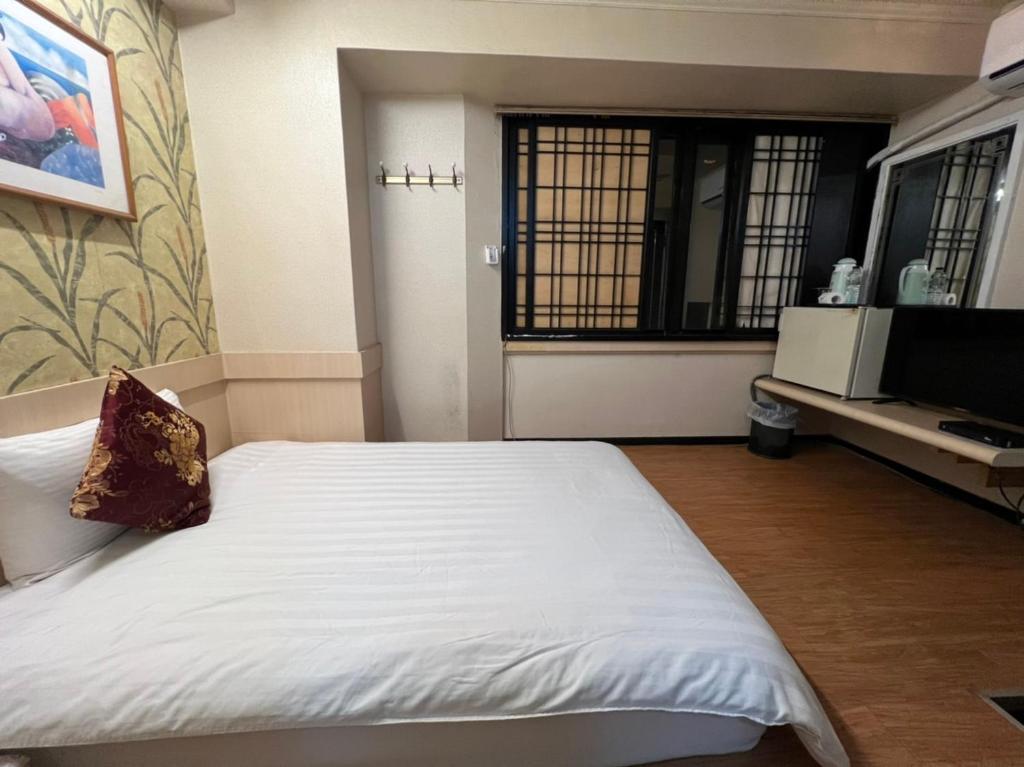 a bedroom with a white bed and a television at Boston Hotel in Chiayi City