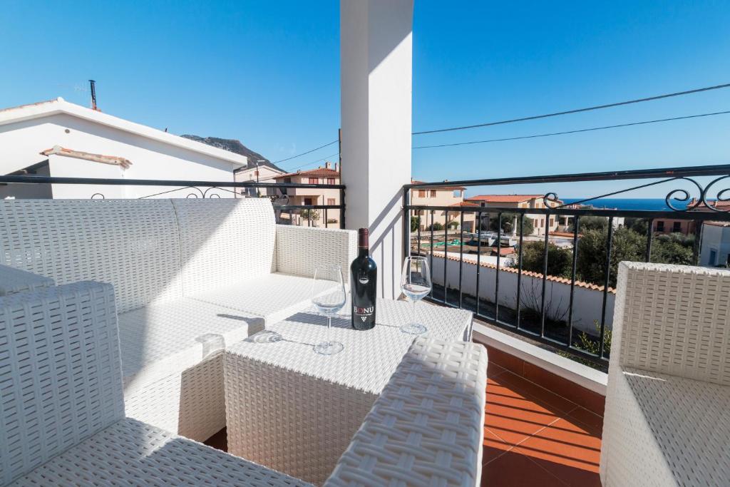 un balcón con sillas blancas y una mesa con copas de vino en Suite Apartment La Punta, en Cala Gonone