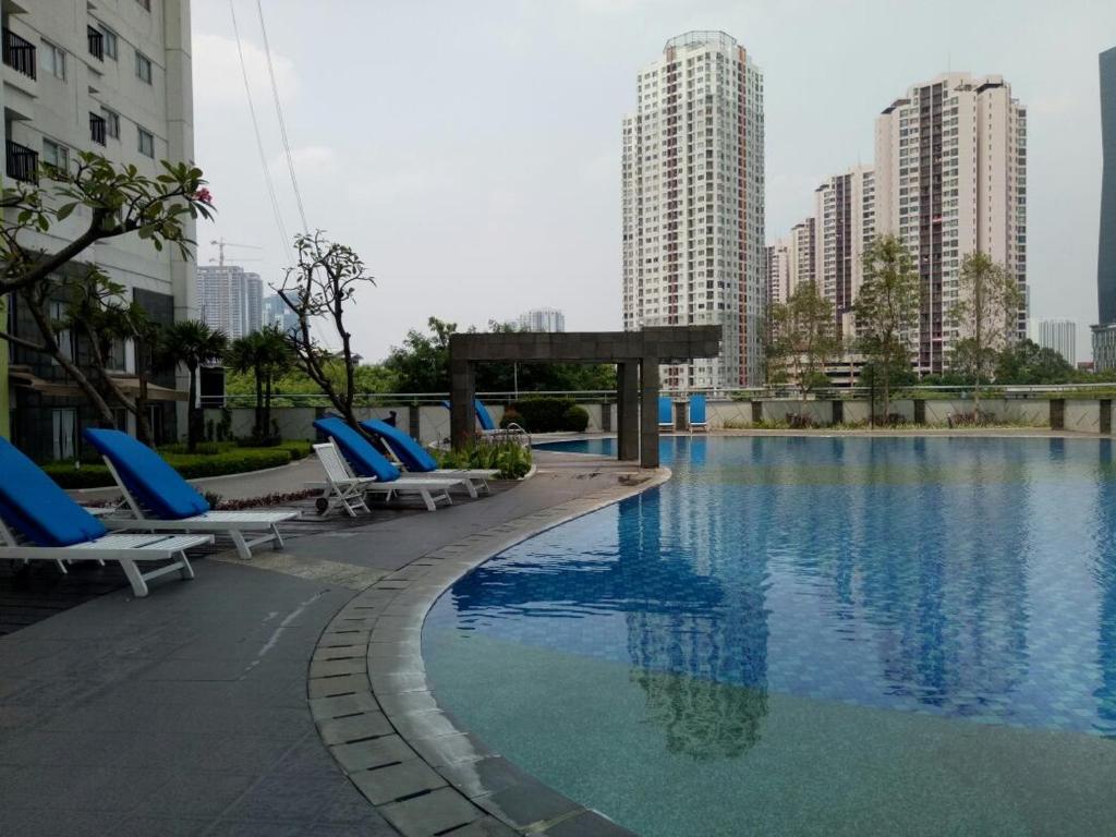 - une piscine avec des chaises longues bleues et des bâtiments dans l'établissement The Wave Apartment, à Jakarta