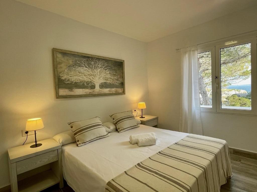 1 dormitorio con 1 cama blanca con 2 lámparas y una ventana en BINIFORCAT, en Cala en Forcat