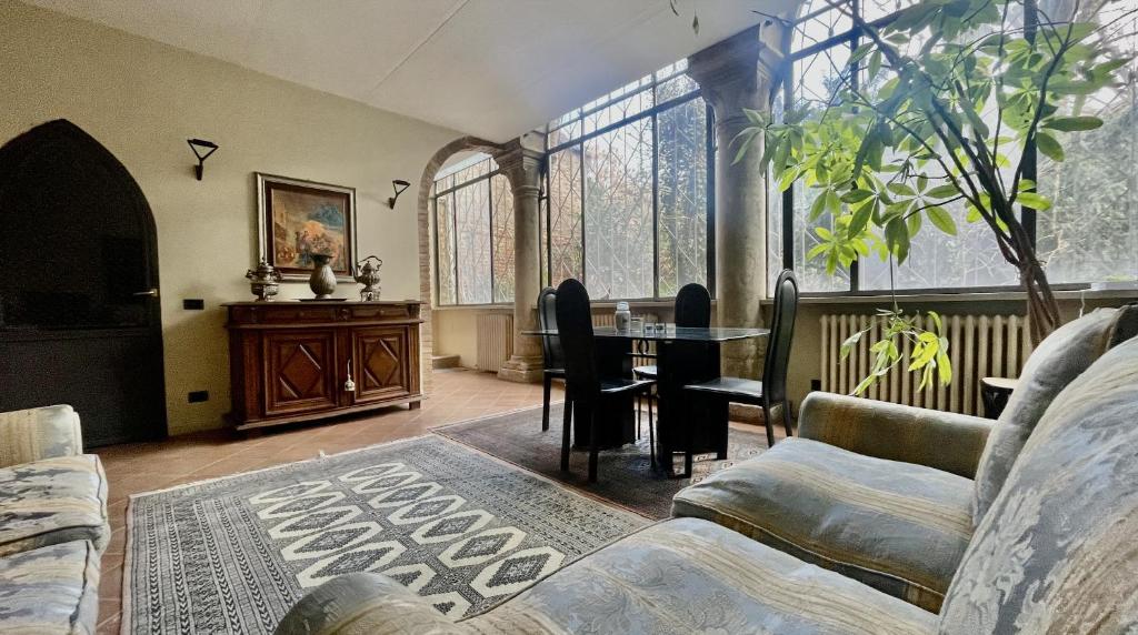 ein Wohnzimmer mit einem Tisch, Stühlen und Fenstern in der Unterkunft Vizi e Virtù in Ferrara
