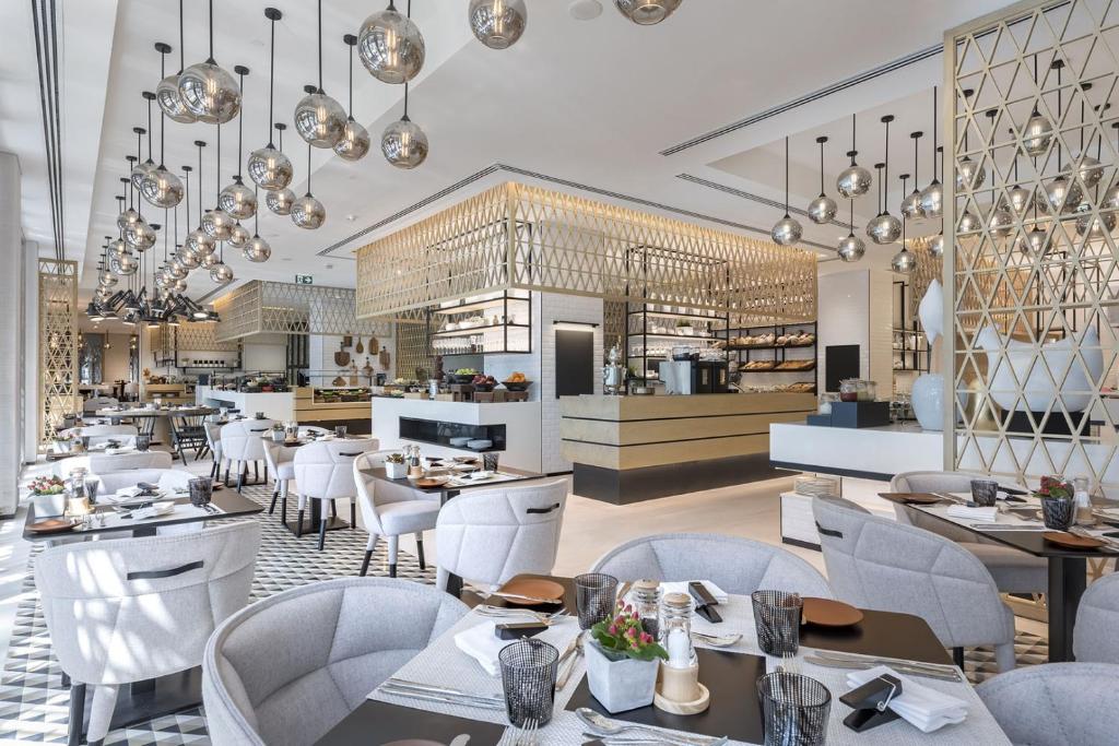 Al Bandar Arjaan by Rotana – Dubai Creek في دبي: مطعم فيه كراسي بيضاء وطاولات ومطبخ
