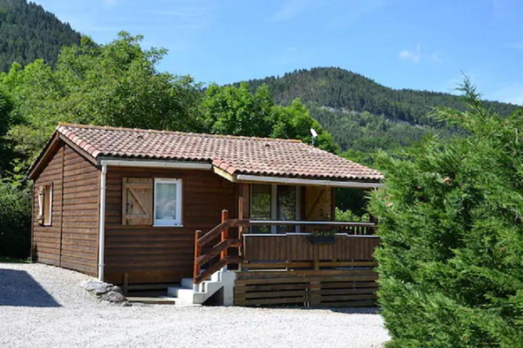 une petite cabine avec une terrasse couverte et des montagnes en arrière-plan dans l'établissement Camping La mare aux fées, à Roquefeuil