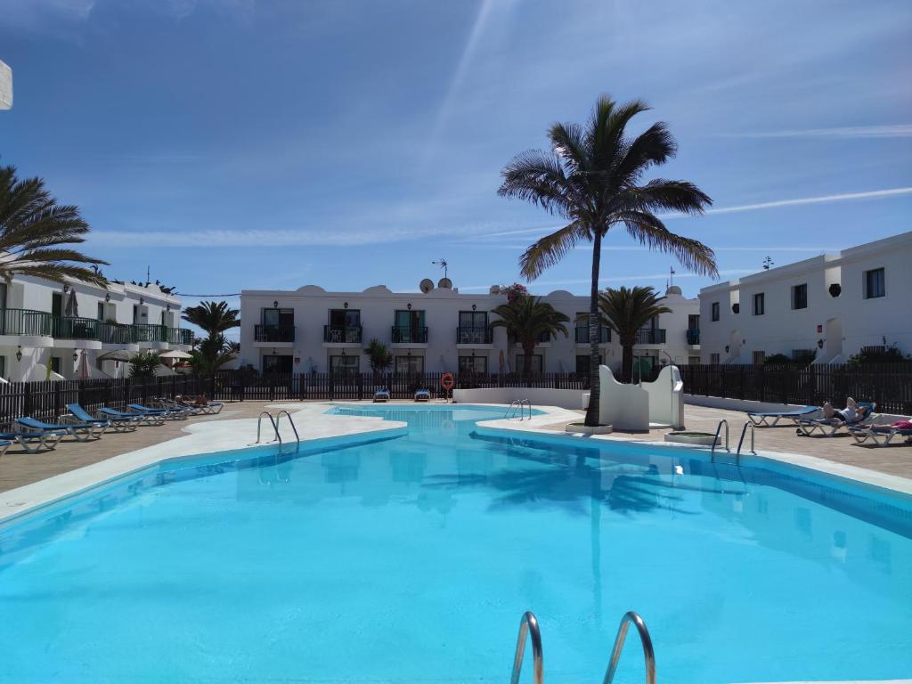 une grande piscine avec des palmiers et des bâtiments dans l'établissement Casa Virginia Corralejo by iRent Fuerteventura, à Corralejo