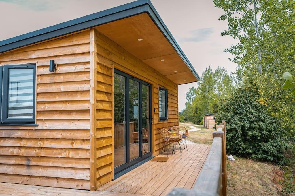 a wooden cabin with a deck with a patio at Lakeside Lodge- 'Lapwing' in Bishampton