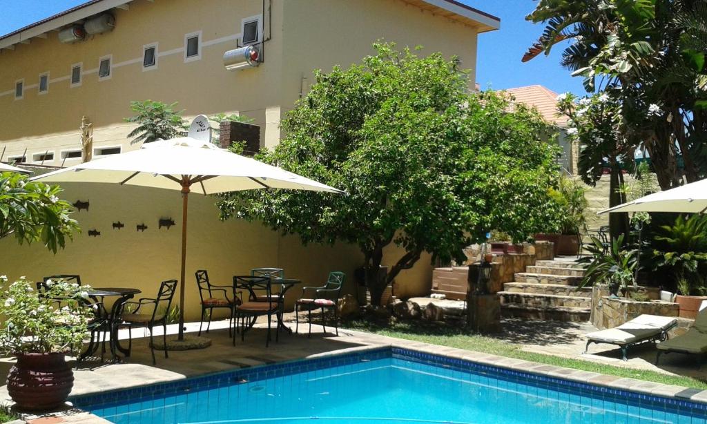 ein Pool mit Tischen und Sonnenschirmen neben einem Gebäude in der Unterkunft hotel pension steiner in Windhoek