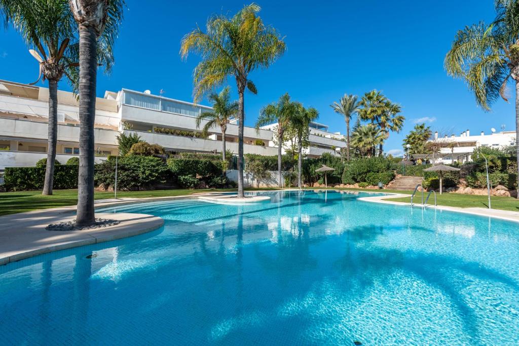 uma grande piscina com palmeiras em frente a um edifício em Apartamento Altos de Banús III em Marbella