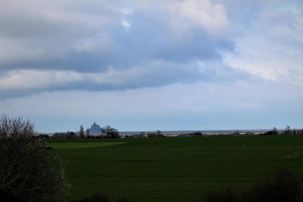 a green field with a church in the distance at Gîtes Bellevue et Mascaret in Courtils