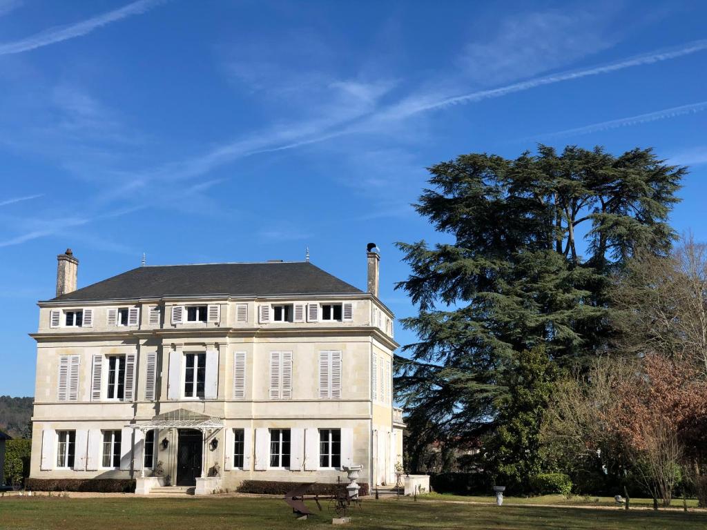 una gran casa blanca con un árbol delante en La maison au cèdre, en Marsac-sur-lʼIsle