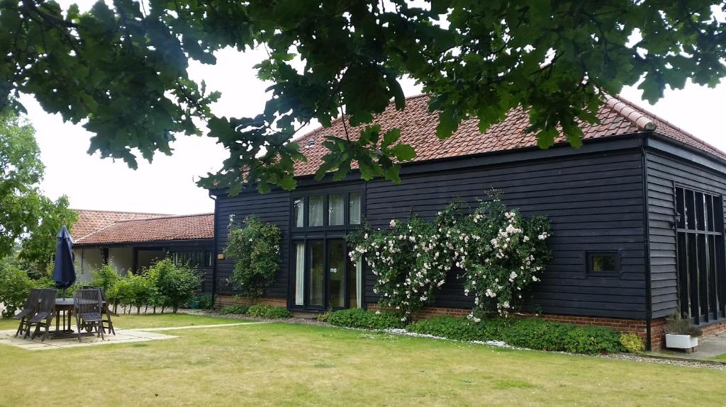 une maison noire avec des tables et des chaises devant elle dans l'établissement Holiday Home Virginia Barn, à East Harling