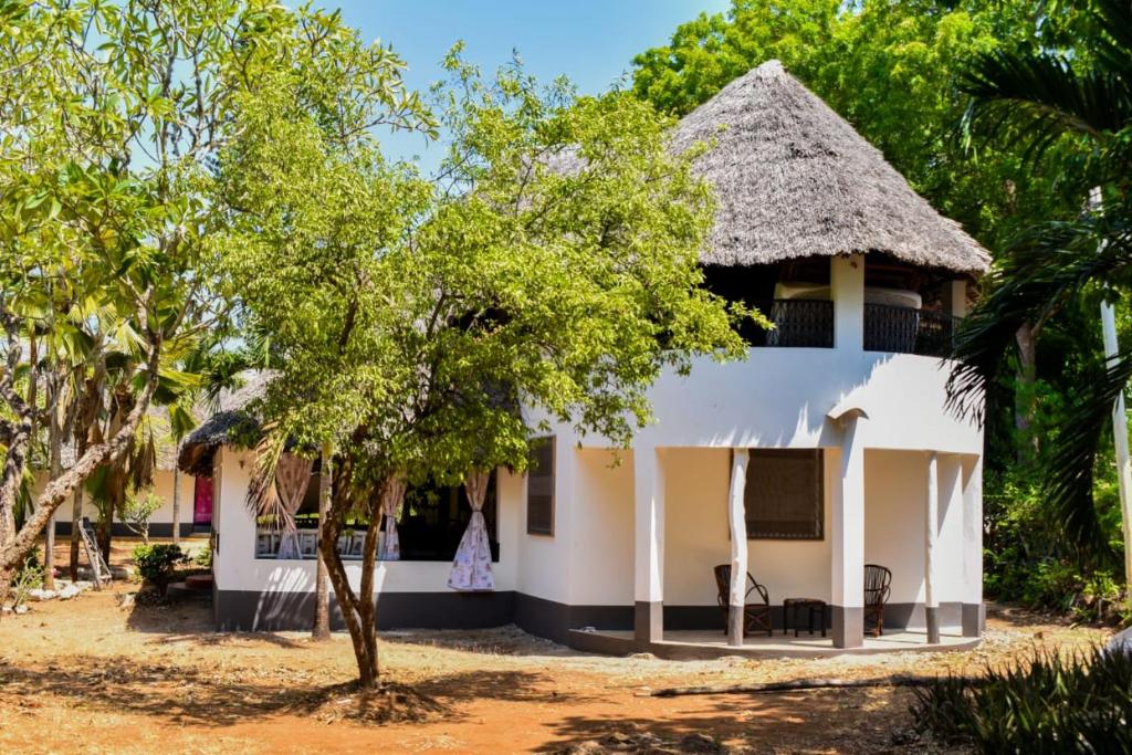 a white house with a thatched roof at Double room in a villa in Diani Beach