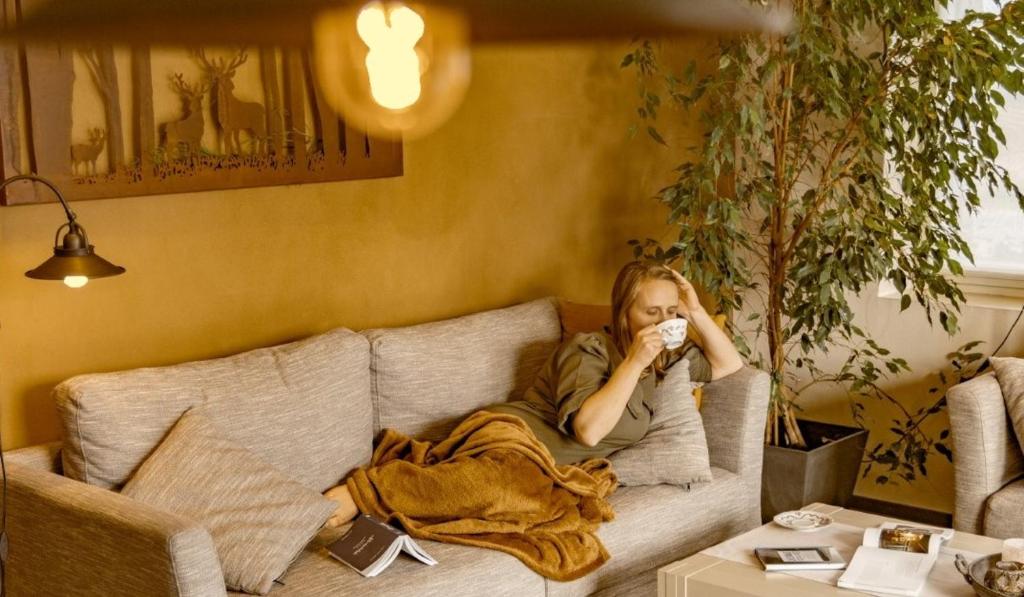 a woman sitting on a couch drinking a cup of coffee at De Zevende Zon in Poperinge