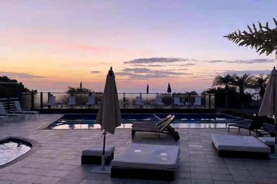 um pátio com um guarda-sol e cadeiras e uma piscina em Apartamento Costão das Gaivotas - Praia do Santinho - Ingleses - Florianópolis em Florianópolis