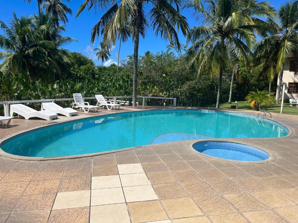 una piscina con sillas y palmeras en DE FRENTE PRA PRAIA Apartamento da Cris Taperapua - Condomínio América Praia Flat, en Porto Seguro