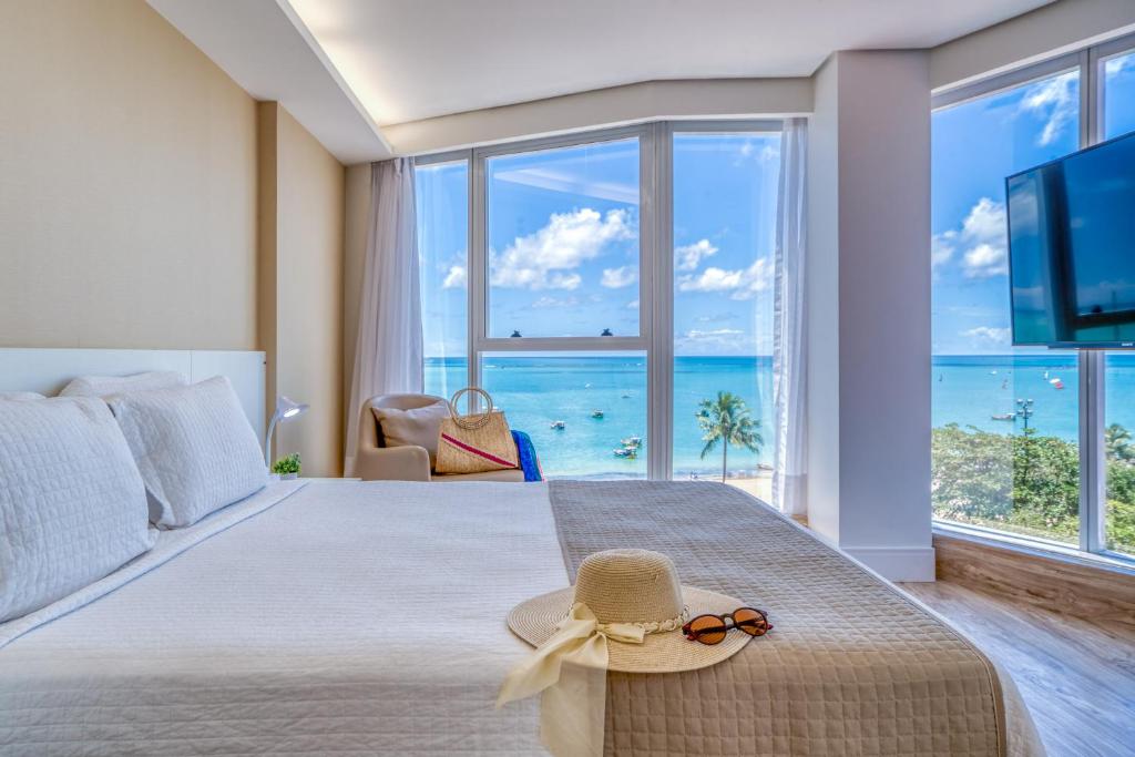 Schlafzimmer mit einem Bett mit Hut und Meerblick in der Unterkunft Hotel Brisa Suítes Pajuçara in Maceió