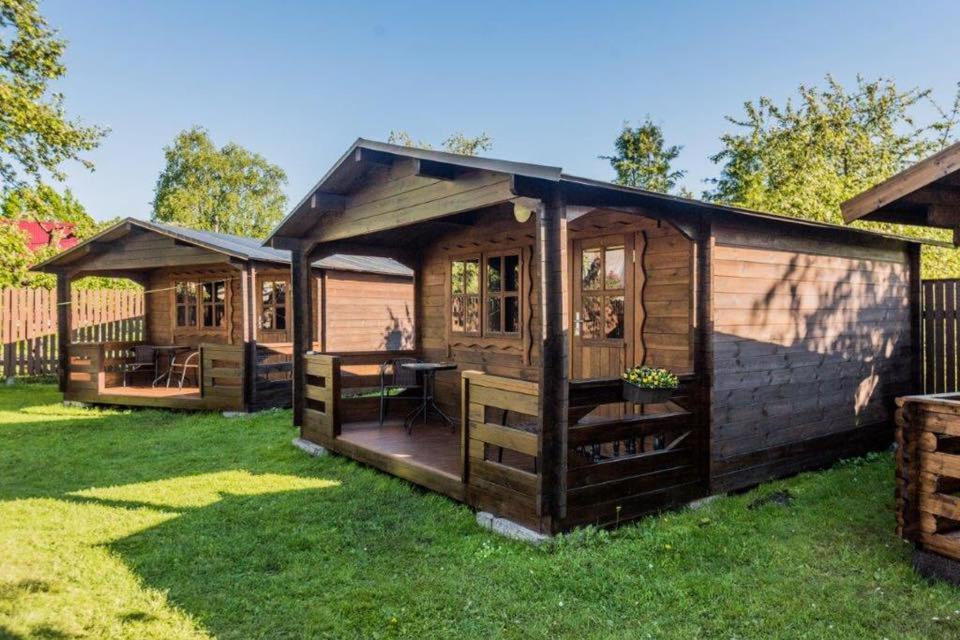 a large wooden cabin with a deck in the grass at Karjamaa Garden Bungalows in Pärnu