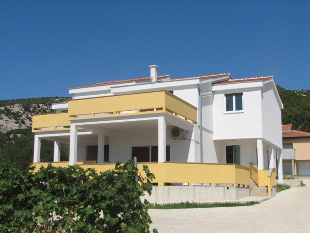 una casa blanca y amarilla con una colina al fondo en Apartments Pijaza, en Rab