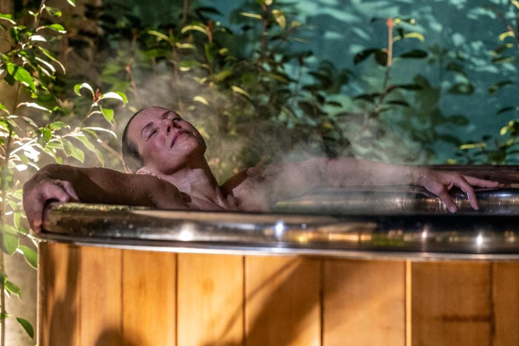 Un homme se posant dans une baignoire avec de la vapeur sortant dans l'établissement Escale Rochelaise B&B, SPA bain nordique et sauna tonneau, à La Rochelle