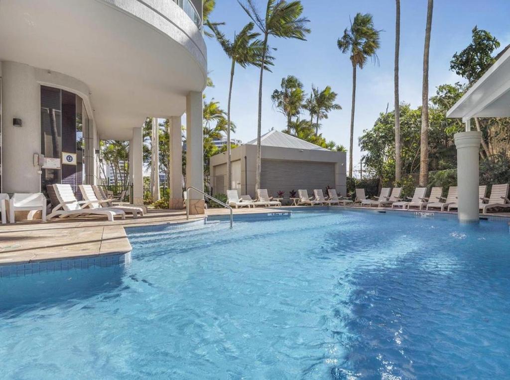 a large swimming pool with chairs and palm trees at Oaks Hotel Deluxe Private Apartment and Studio - Ocean Views in Gold Coast