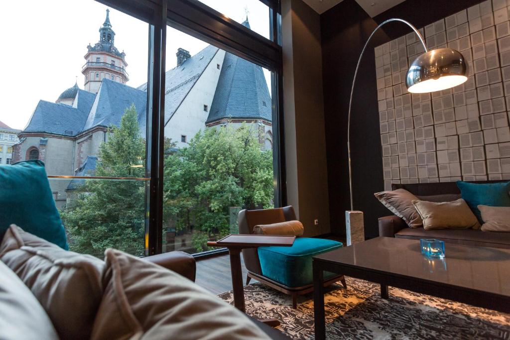 a living room with a couch and a table and a large window at Motel One Leipzig-Augustusplatz in Leipzig