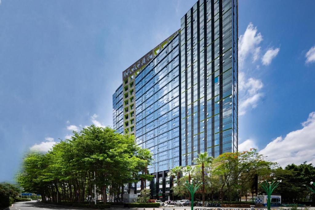 een hoog glazen gebouw met bomen ervoor bij Atour Hotel Shenzhen Nanshan Qianhai Yiche in Shenzhen