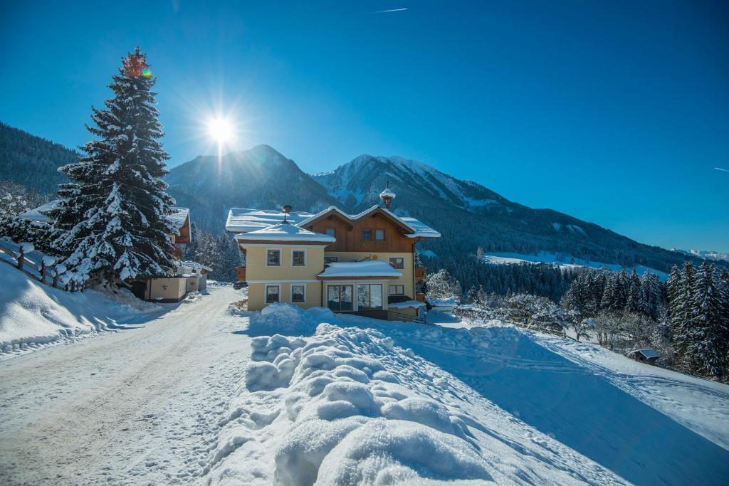 une maison recouverte de neige avec le soleil en arrière-plan dans l'établissement Ferien Bauernhof Maurachhof, à Sankt Johann im Pongau