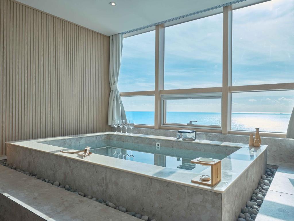a large bath tub in a room with a large window at UH SUITE THE HAEUNDAE in Busan