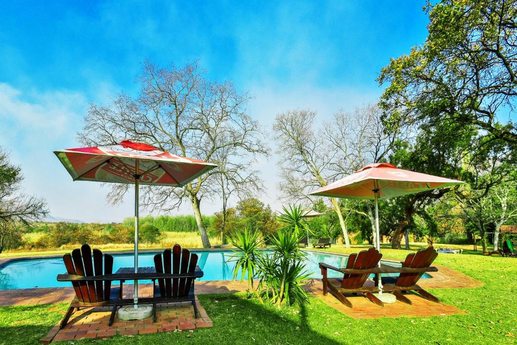 two umbrellas and chairs next to a swimming pool at The Venue Country Hotel & Spa in Hartbeespoort