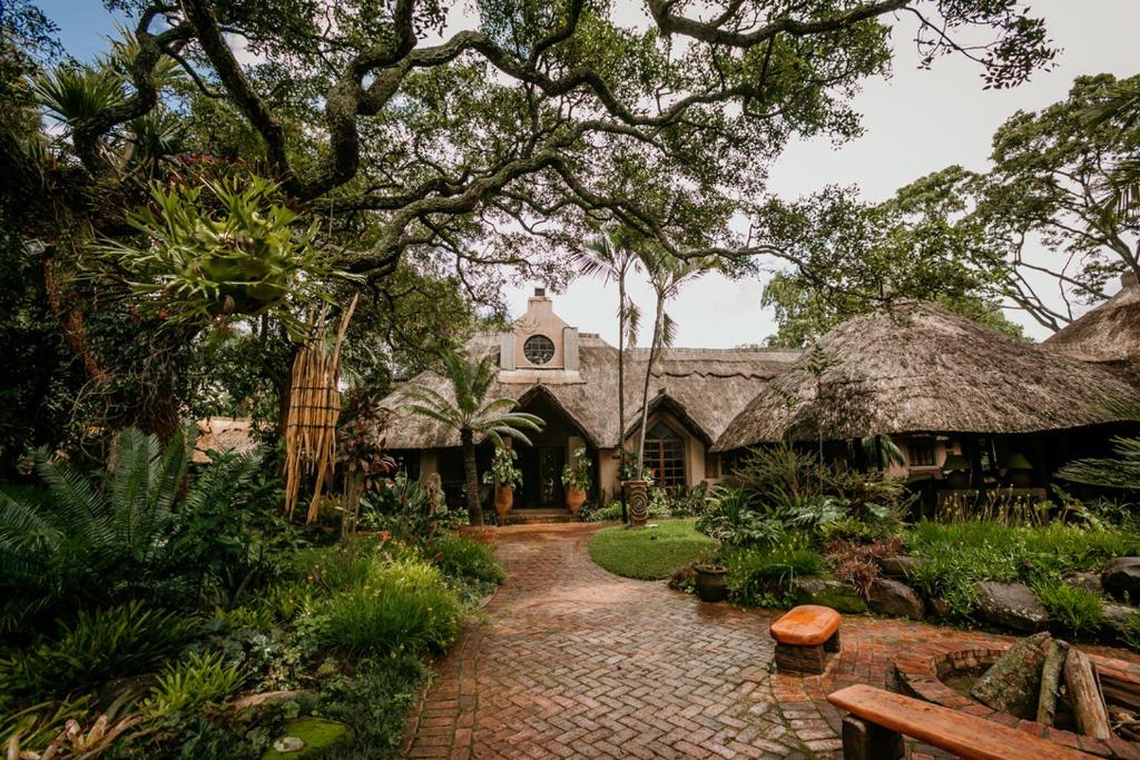 atropical house with a brick walkway and trees at Amanzi Lodge in Harare