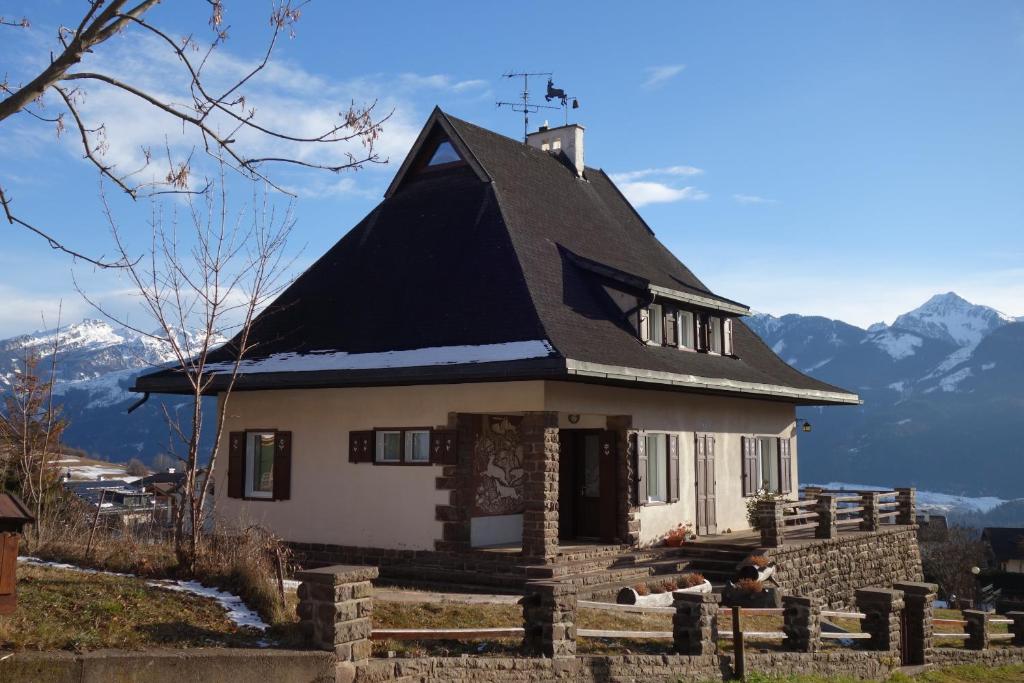 a house with a black roof with mountains in the background at Villa Molteni, Ville di Fiemme, Varena in Varena