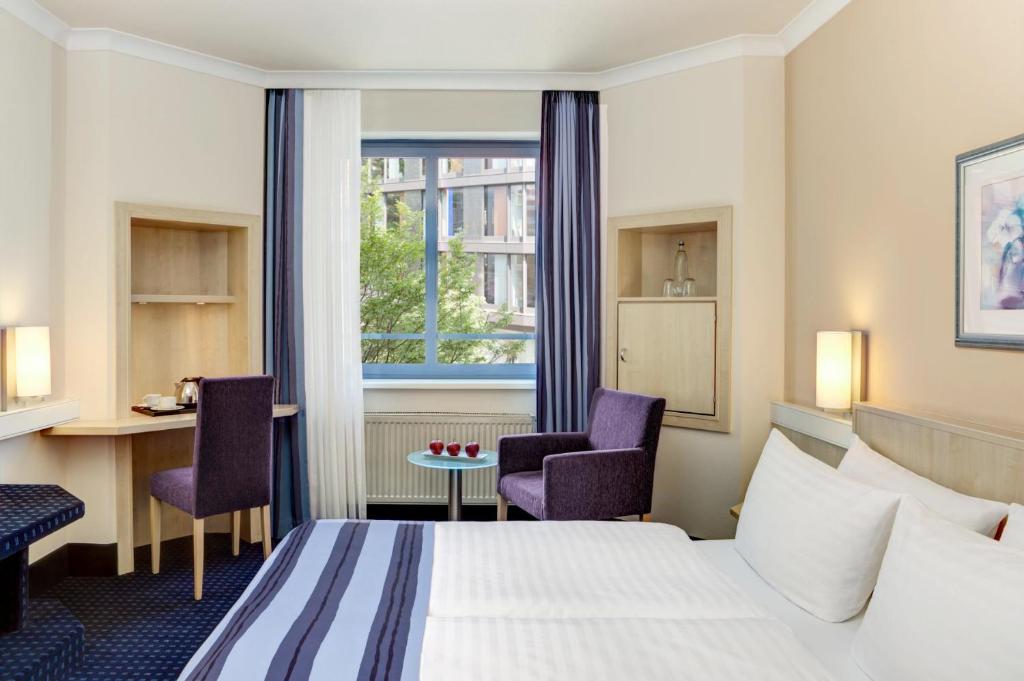 ein Hotelzimmer mit einem Bett, zwei Stühlen und einem Fenster in der Unterkunft IntercityHotel Nürnberg in Nürnberg