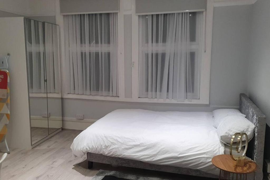 a bedroom with a bed with white sheets and windows at Studio flat in lovely Alexandra Palace London in London