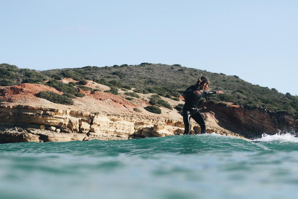 a man riding a wave on a surfboard in the water at Aldeia Caiçara Surf House in Sagres