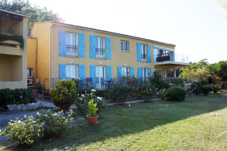 een groot huis met blauwe ramen en een tuin bij Hotel Les Cavalets in Bauduen