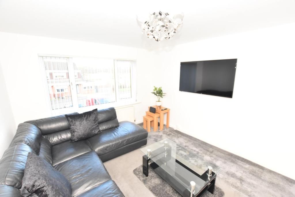 sala de estar con sofá de cuero y TV de pantalla plana en 3 Bedroom Apartment in a Quiet Location, en Airdrie