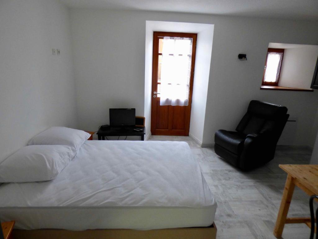 a bedroom with a white bed and a black chair at Auberge Les Grillons in Meyras